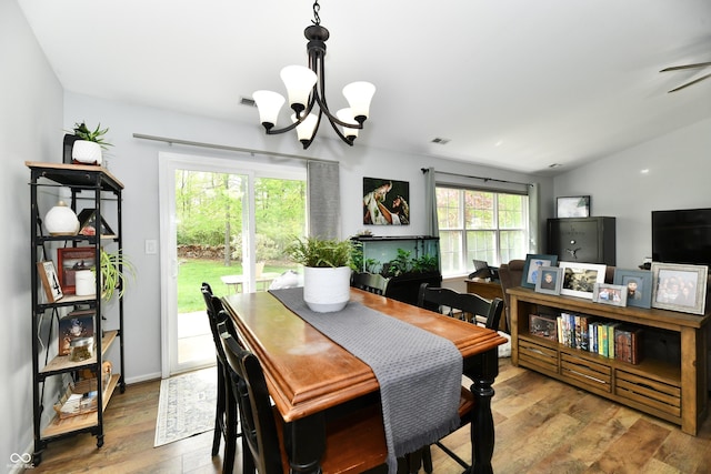 dining area with lofted ceiling, wood-type flooring, ceiling fan with notable chandelier, and visible vents