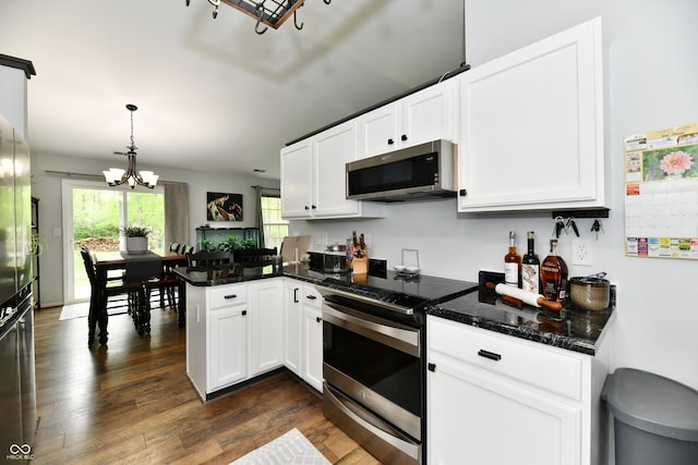 kitchen with a peninsula, stainless steel appliances, a notable chandelier, white cabinets, and dark wood-type flooring