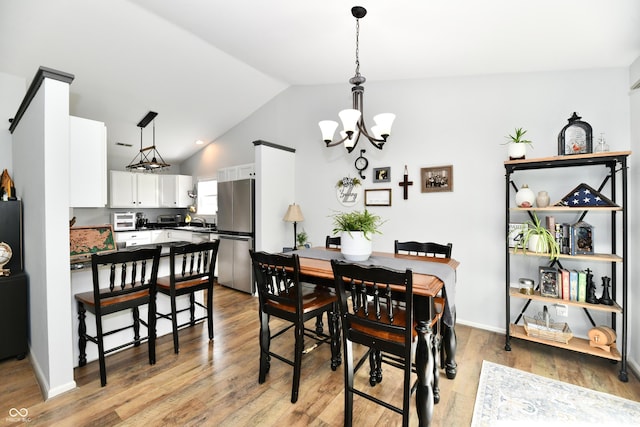 dining room featuring an inviting chandelier, lofted ceiling, and light wood-type flooring