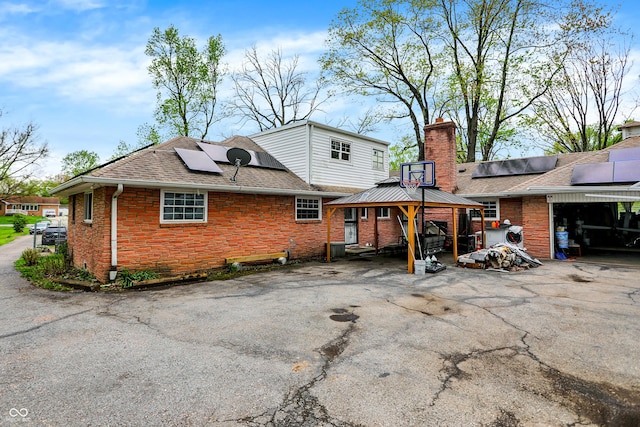 3975 Denwood Dr, Indianapolis, IN 46226 - back of house with a gazebo, roof mounted solar panels, a chimney, roof with shingles, and brick siding