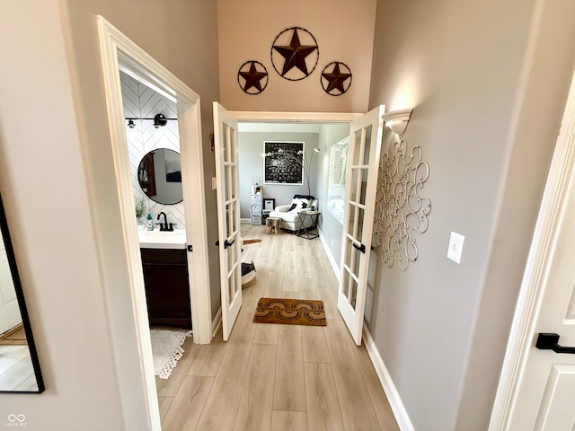 hall with french doors, light wood finished floors, a sink, and baseboards