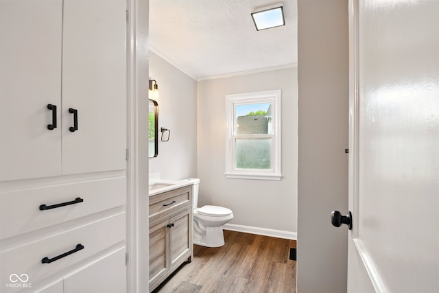 bathroom featuring wood finished floors, crown molding, vanity, toilet, and baseboards