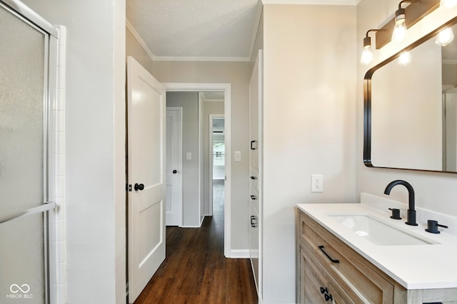 full bath featuring wood finished floors, ornamental molding, vanity, a shower with shower door, and baseboards