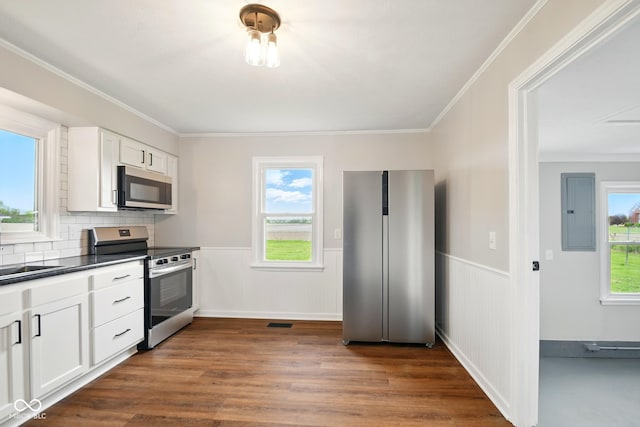 kitchen featuring appliances with stainless steel finishes, electric panel, dark countertops, a wainscoted wall, and dark wood-style flooring