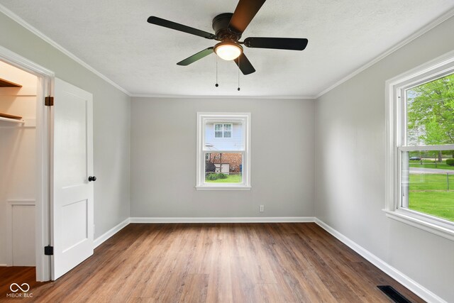unfurnished bedroom with multiple windows, wood finished floors, baseboards, and crown molding