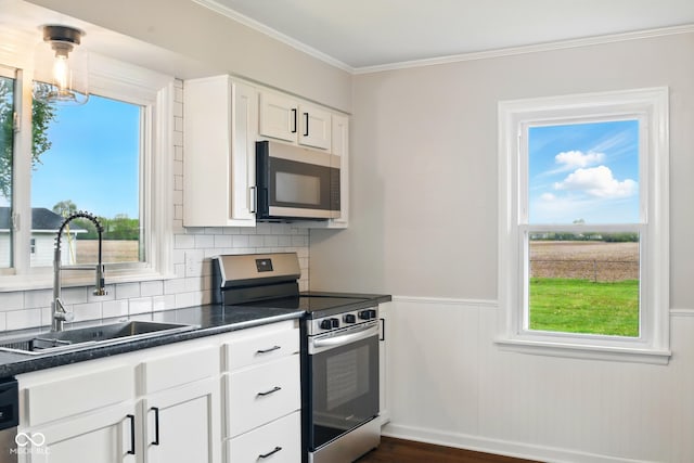 kitchen featuring appliances with stainless steel finishes, a sink, dark countertops, white cabinetry, and a wainscoted wall