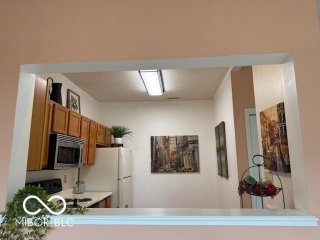 8002 Windham Lake Way Unit 33, Indianapolis, IN 46214 - kitchen with stainless steel microwave, range, brown cabinets, freestanding refrigerator, and light countertops