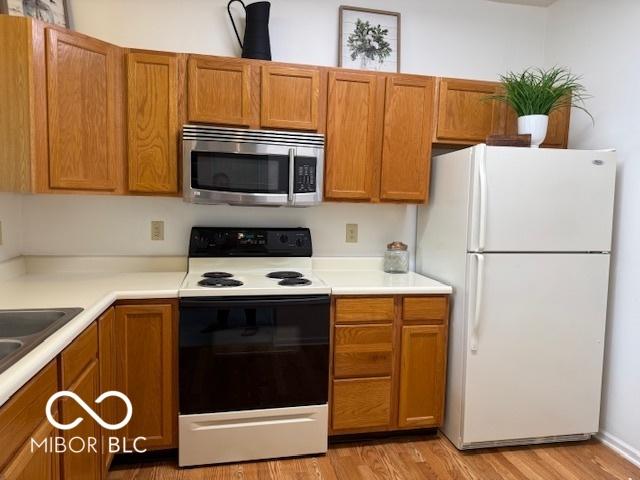 8002 Windham Lake Way Unit 33, Indianapolis, IN 46214 - kitchen with freestanding refrigerator, stainless steel microwave, range with electric stovetop, light wood-style floors, and brown cabinetry