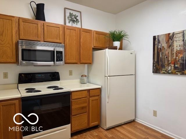 8002 Windham Lake Way Unit 33, Indianapolis, IN 46214 - kitchen with stainless steel microwave, electric stove, freestanding refrigerator, light wood-style flooring, and brown cabinetry