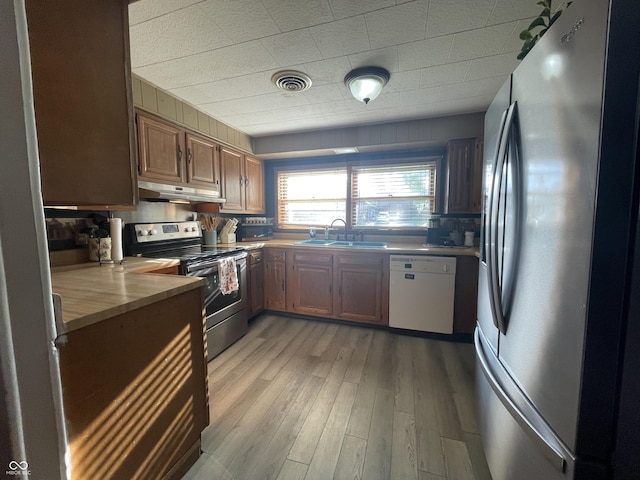 kitchen with under cabinet range hood, visible vents, a sink, light wood-style floors, and stainless steel appliances