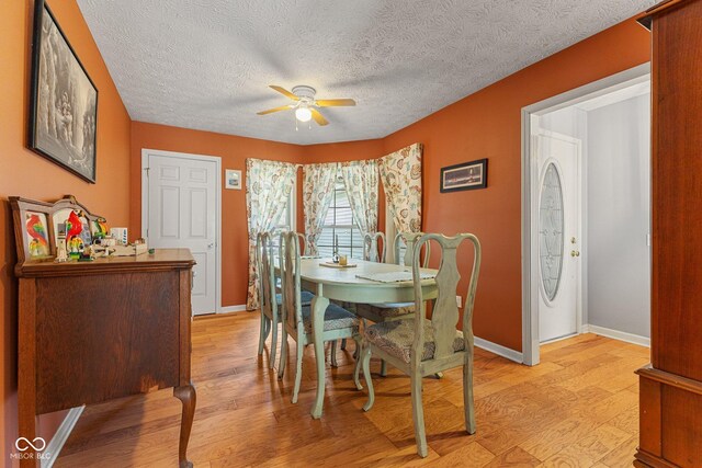 dining area with ceiling fan, light wood-style floors, baseboards, and a textured ceiling
