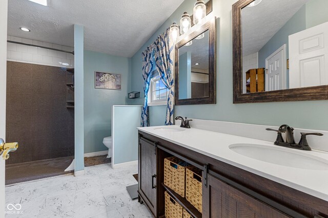 full bath with a textured ceiling, a tile shower, double vanity, toilet, and baseboards