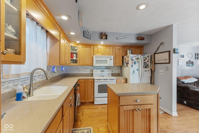kitchen featuring white appliances, a textured ceiling, light wood finished floors, backsplash, and a sink