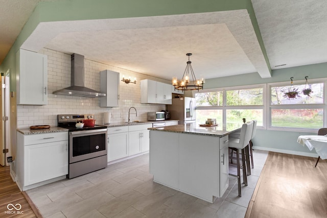 kitchen with appliances with stainless steel finishes, wall chimney exhaust hood, a textured ceiling, a chandelier, and a sink