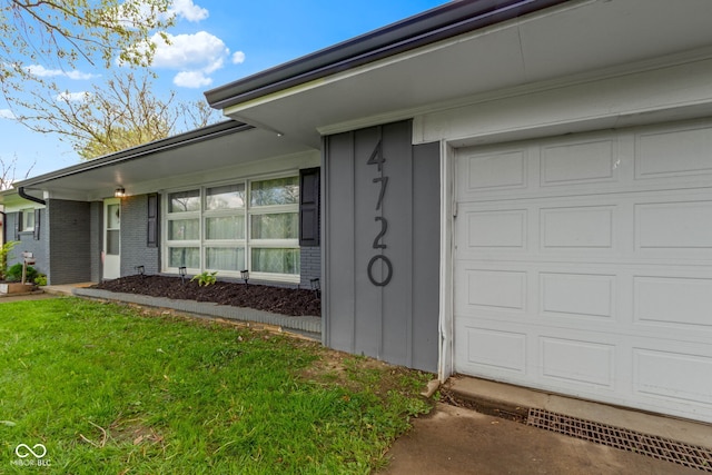 entrance to property with a garage, brick siding, and a yard