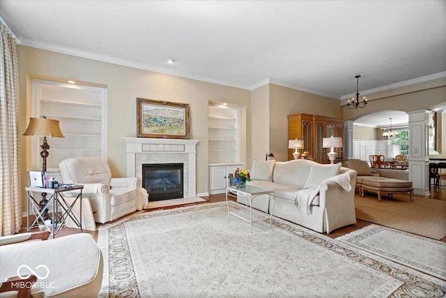 living area featuring a chandelier, ornate columns, built in shelves, wood finished floors, and a high end fireplace