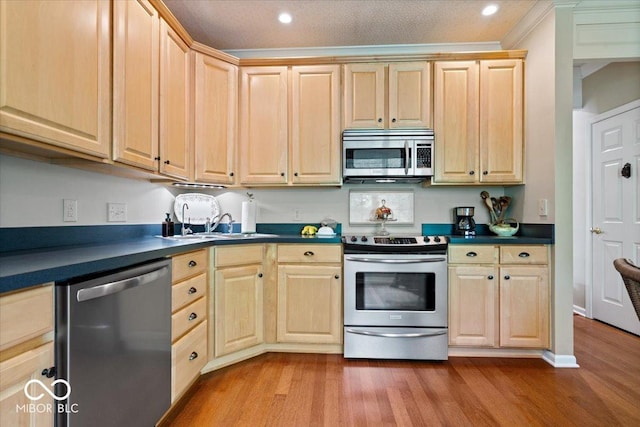 kitchen featuring stainless steel appliances, light brown cabinetry, dark countertops, wood finished floors, and recessed lighting