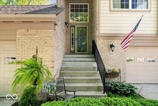 doorway to property featuring brick siding, an attached garage, and a shingled roof
