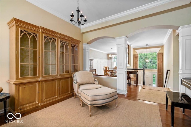 sitting room featuring arched walkways, a chandelier, ornate columns, ornamental molding, and wood finished floors