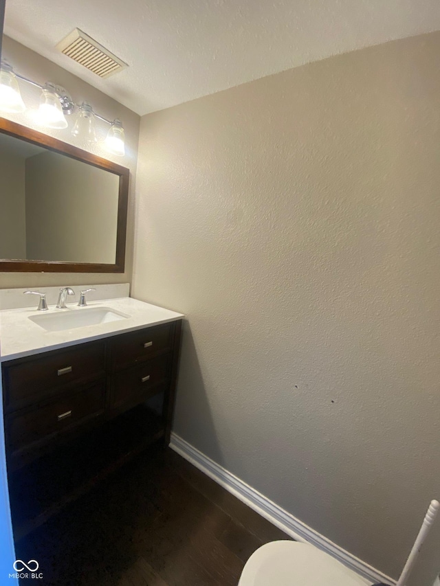 half bathroom with toilet, wood finished floors, visible vents, baseboards, and vanity