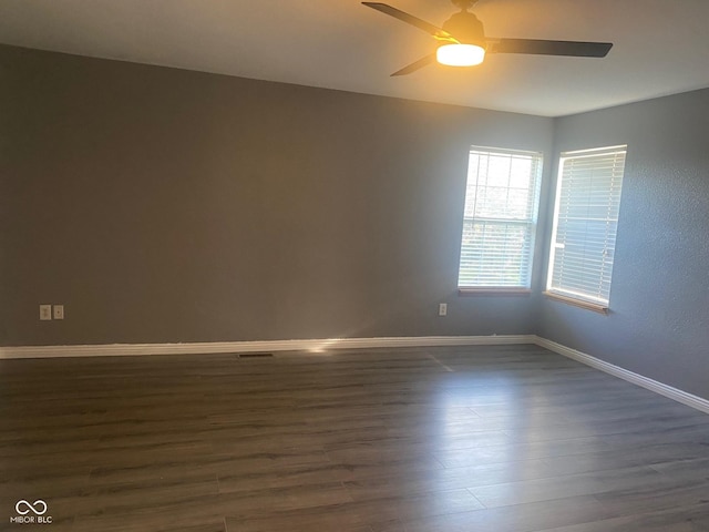 spare room with baseboards, ceiling fan, and dark wood-type flooring