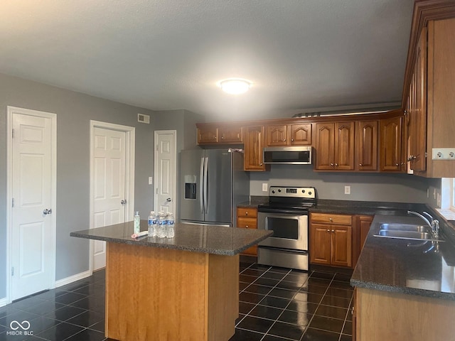 kitchen with a sink, dark tile patterned floors, a center island, and appliances with stainless steel finishes
