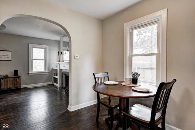 dining space with dark wood-style flooring, baseboards, a fireplace, and arched walkways
