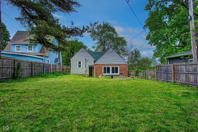 rear view of property featuring a yard, brick siding, and a fenced backyard