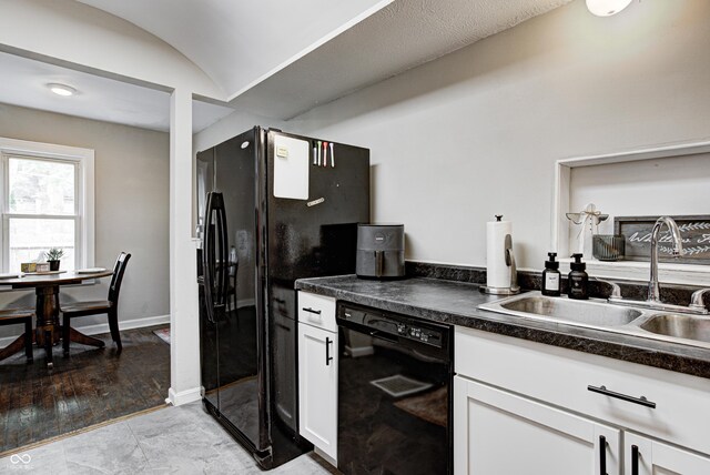 kitchen featuring dark countertops, white cabinetry, black appliances, and a sink