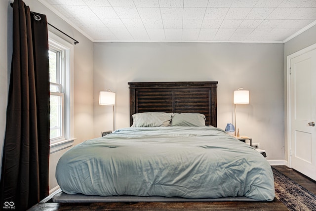 bedroom with baseboards, multiple windows, crown molding, and wood finished floors