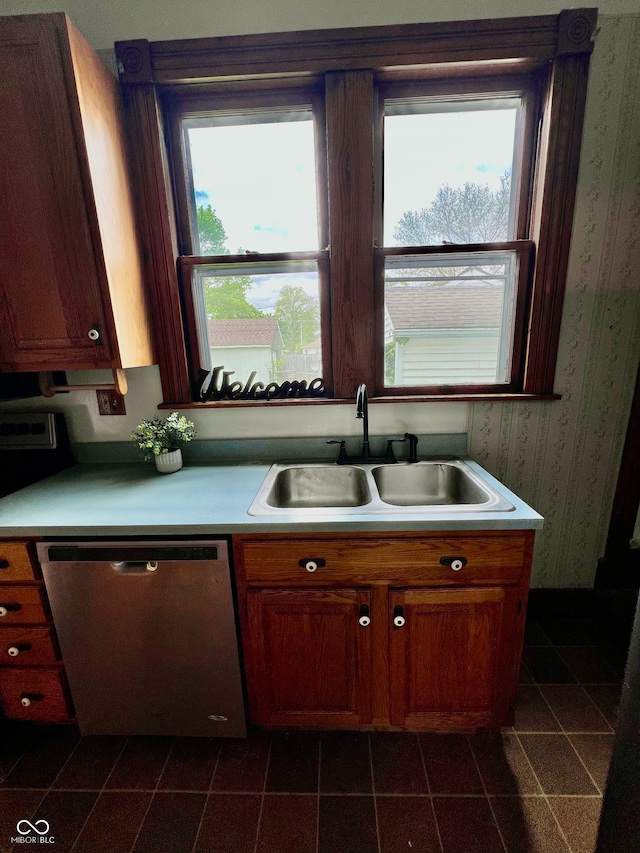 kitchen featuring dark tile patterned floors, a sink, wallpapered walls, stainless steel dishwasher, and light countertops
