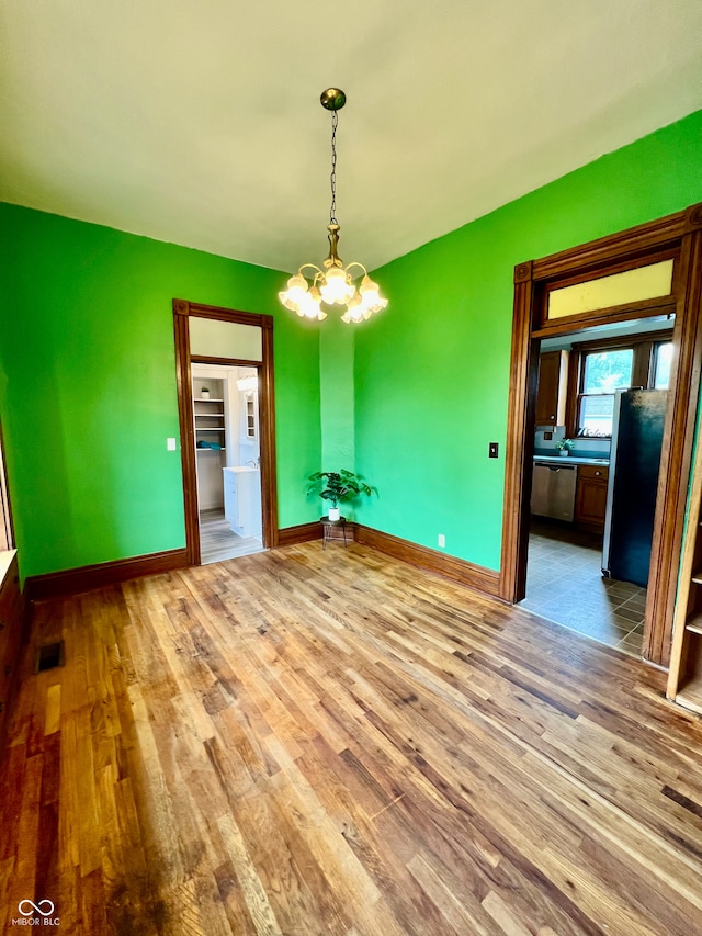 unfurnished dining area with a notable chandelier, baseboards, visible vents, and wood finished floors