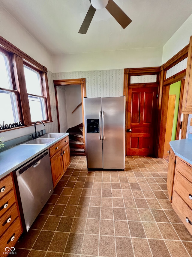 kitchen with a ceiling fan, wallpapered walls, a sink, dark tile patterned flooring, and appliances with stainless steel finishes