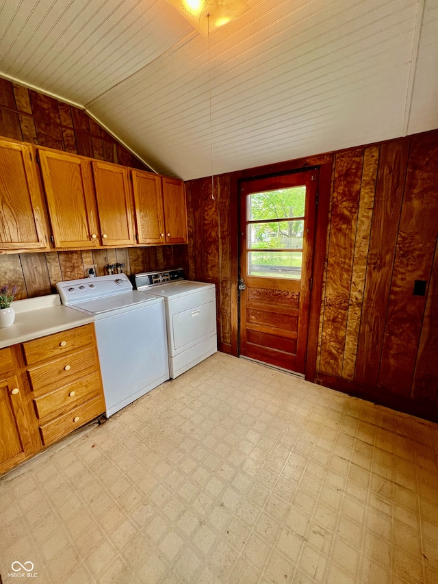 washroom featuring light floors, wood walls, independent washer and dryer, and cabinet space