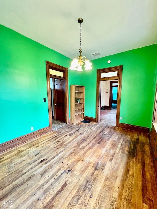 unfurnished dining area with a chandelier, baseboards, visible vents, and wood finished floors