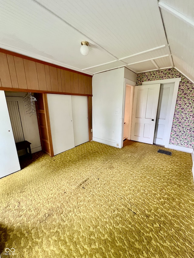 unfurnished bedroom with carpet floors, visible vents, wallpapered walls, and vaulted ceiling