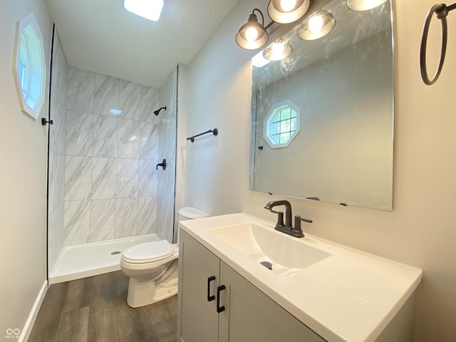 full bath featuring vanity, toilet, wood finished floors, and a tile shower