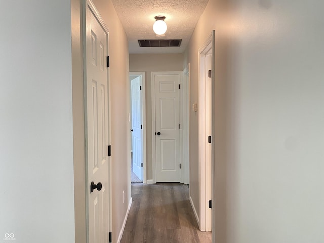 hallway featuring baseboards, dark wood finished floors, visible vents, and a textured ceiling