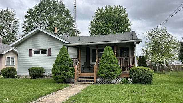 view of front of property featuring a front lawn, a shingled roof, covered porch, and fence