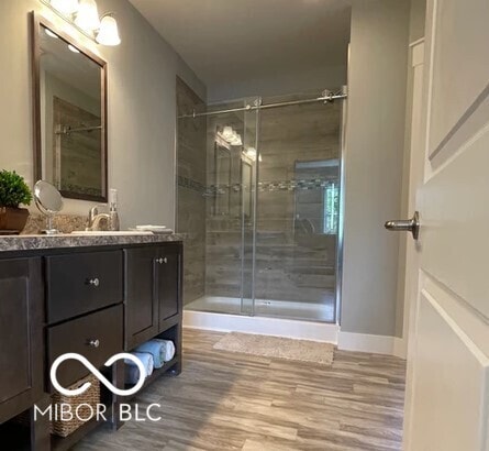 full bathroom featuring a stall shower, vanity, baseboards, and wood finished floors