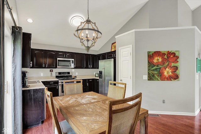 kitchen with stainless steel appliances, a chandelier, wood finished floors, light countertops, and high vaulted ceiling