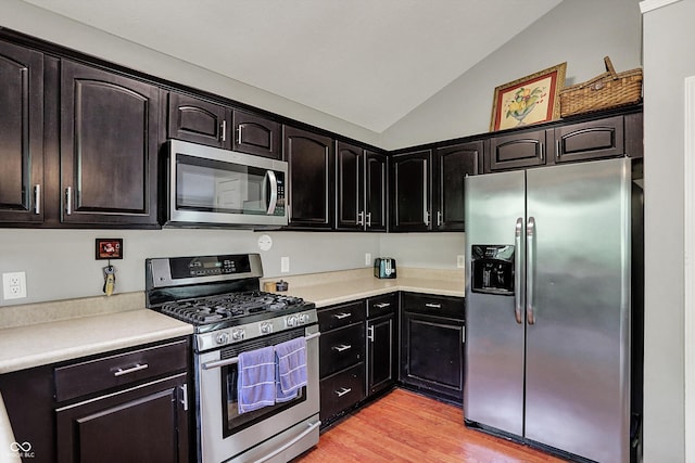kitchen with stainless steel appliances, vaulted ceiling, light countertops, and light wood-style floors