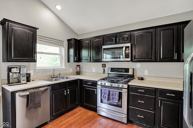 kitchen featuring stainless steel appliances, a sink, vaulted ceiling, dark cabinetry, and light countertops