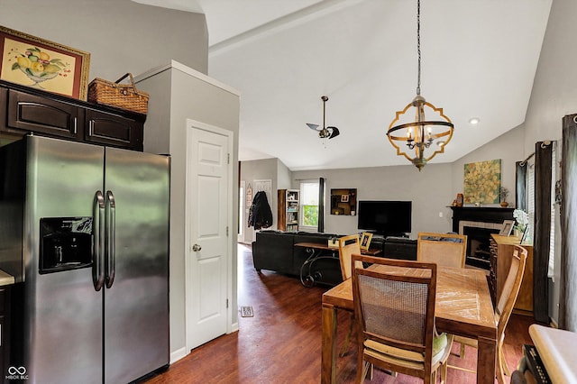 dining space with vaulted ceiling, dark wood-style floors, a chandelier, and a fireplace
