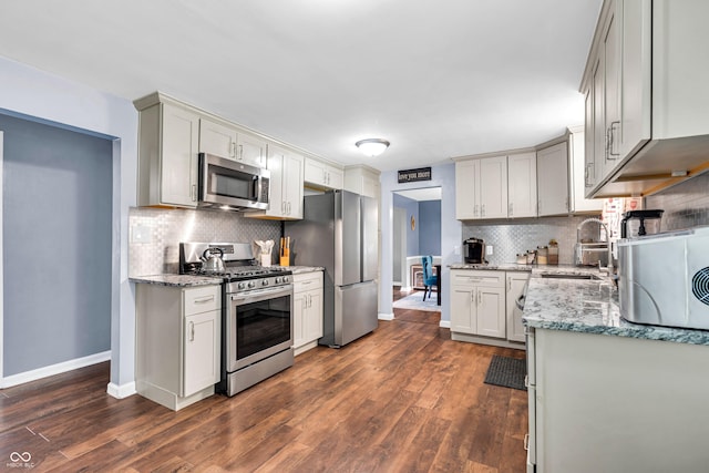 kitchen with stainless steel appliances, baseboards, backsplash, a sink, and dark wood-type flooring