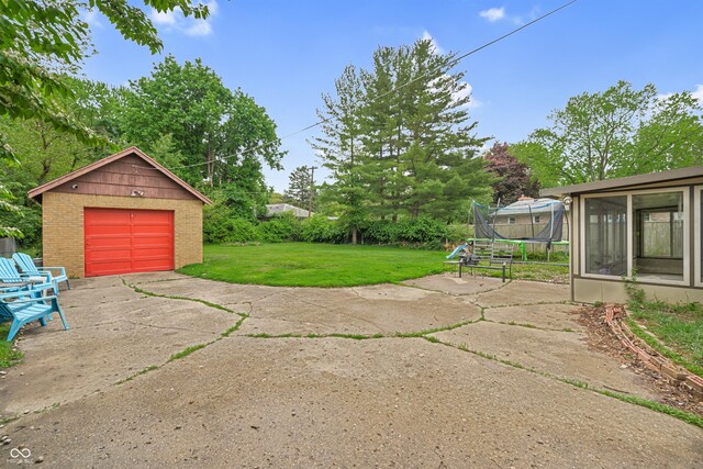 view of green lawn featuring a trampoline, driveway, a garage, an outbuilding, and a sunroom