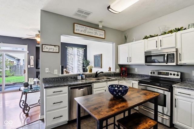7045 Gavin Dr, Indianapolis, IN 46217 - kitchen with stainless steel appliances, a sink, dark countertops, white cabinets, and dark tile patterned floors