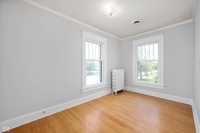 spare room with radiator, baseboards, light wood-type flooring, and crown molding