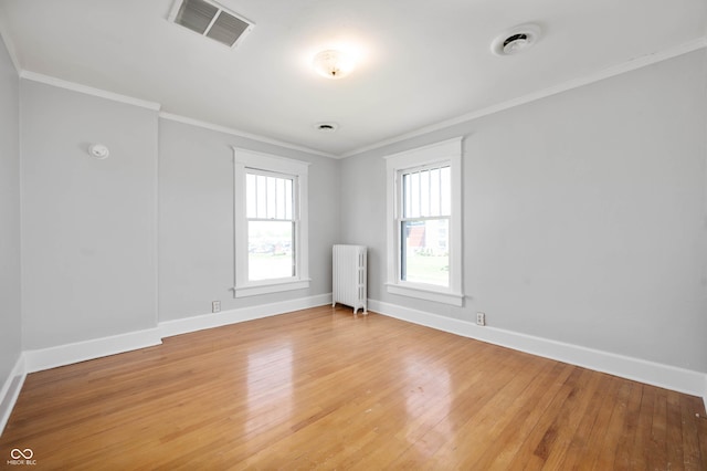 empty room featuring radiator heating unit, baseboards, light wood-style flooring, and crown molding