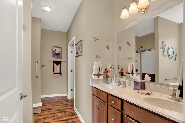 full bath with a shower with door, double vanity, a sink, and wood finished floors